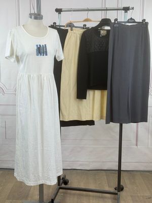 une robe blanche posée sur un portant, à côté d'un pantalon noir