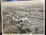 black and white photo of an old airplane flying over a rural area