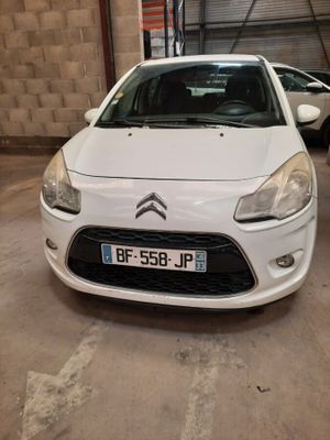 La voiture blanche est garée dans un garage, avec d'autres voitures en arrière-plan.