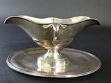 a silver sauce boat on a silver plate on a black table