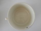 underside view of a white cup with a black handle on a white table