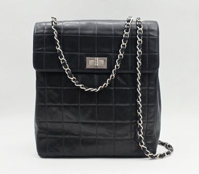 un sac à main en cuir noir muni d'une bandoulière en chaîne, sur fond blanc