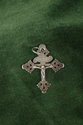 une croix en argent ornée d'un oiseau, posée sur un tissu vert