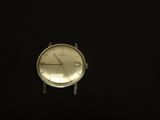 une montre argentée posée sur une surface noire, à côté d'une télécommande