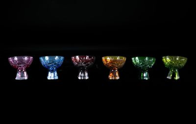 six vases en verre de couleurs différentes alignés sur un fond noir