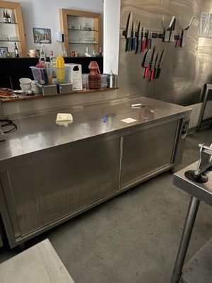 un grand plan de travail en inox dans une cuisine où de nombreux couteaux sont accrochés au mur