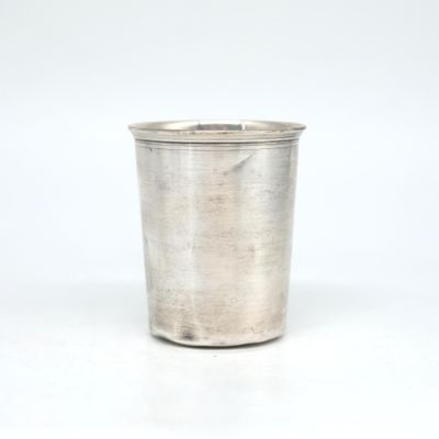 une vieille coupe en argent munie d'une anse, posée sur une surface blanche