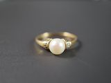 gros plan d'une bague en or avec une perle et des diamants