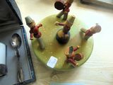 Plusieurs figurines sont posées sur une assiette, accompagnées de cuillères et d'un repose-cuillère, sur une table.