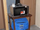 a microwave sitting on a small table with a blue bag on it