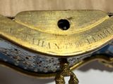 a gold and blue clock on a stand on a white wall