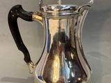 silver plated coffee pot with black handle on white background