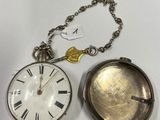 une montre de poche en argent posée à côté d'une chaîne à laquelle est accrochée une clé