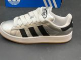 silver and black adidas sneakers with white soles on a grey surface