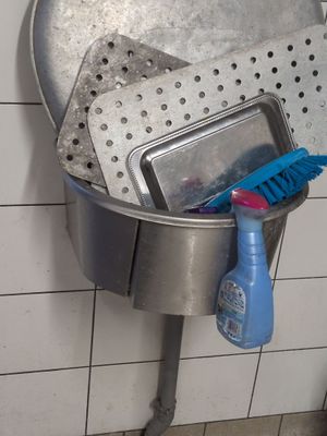 a metal sink with a bucket of cleaning supplies inside of it