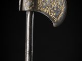 a close up of a silver and gold axe on a black background