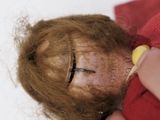 a hand holding a needle to a doll ' s face