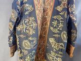 une veste bleue ornée de motifs dorés et rouges, suspendue à un cintre