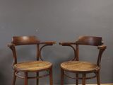 two wooden chairs with wicker seats in front of a gray wall