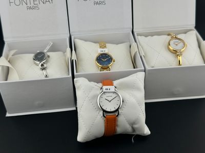 trois montres dans une boîte blanche, avec des bracelets orange, posées sur une table noire