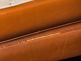 a close up of a brown leather couch with a white pillow