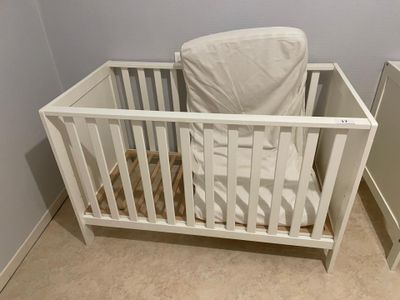 a white crib with a white sheet on it in the corner of a room