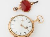 a gold pocket watch with a red stone on the face