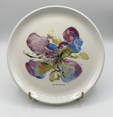 une assiette blanche sur laquelle est peinte une fleur violette et bleue