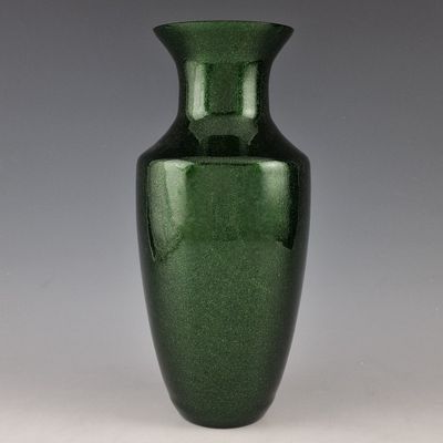 un vase vert posé sur une table blanche, près d'un mur gris