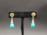 une paire de boucles d'oreilles turquoise et or posées sur un présentoir noir