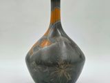 un vase noir et orange posé sur une surface blanche
