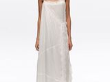 a woman wearing a white dress and sandals standing in front of a white background