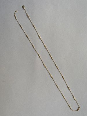un collier en or dont la chaîne a été coupée et qui repose sur une surface blanche