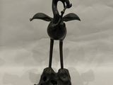une vieille statue en bronze représentant un oiseau perché sur un rocher, sur fond blanc