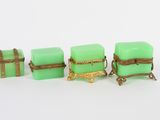 trois petites boîtes vertes ornées de bordures dorées et dotées de poignées, posées sur un fond blanc