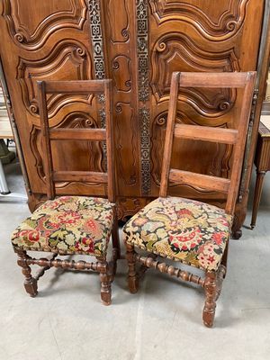 deux chaises en bois aux assises rembourrées de motifs floraux, placées devant une grande porte en bois
