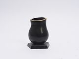 vase noir reposant sur un socle en bois, posé sur une surface blanche