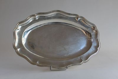assiette en argent plaqué à bord festonné, posée sur un socle, sur fond blanc