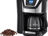 une cafetière noire et argentée à côté d'un tas de grains de café