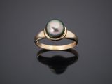 a black pearl and gold ring on a black surface