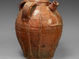un vieux vase marron muni de deux anses, sur un fond gris
