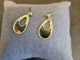 une paire de boucles d'oreilles dorées et noires posées sur un coussin