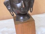 a bronze statue of a buddha head on a wooden block
