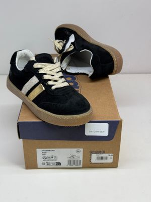une paire de baskets noires et dorées posées sur une boîte en carton