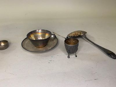 une tasse et une soucoupe en argent, ainsi que des cuillères, posées sur une table