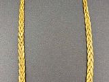 a gold necklace with a braid design on a black surface