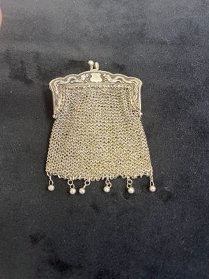 a silver mesh purse with pearls hanging from it on a black surface
