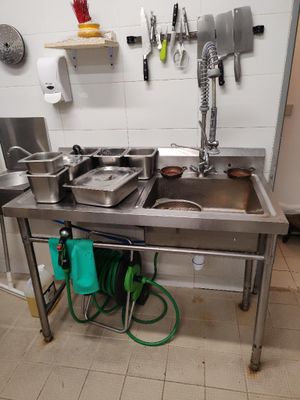 une cuisine avec un évier en inox et un tuyau d'arrosage vert posé par terre