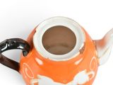 an orange and white tea pot with a black handle
