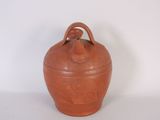 an orange clay jar with a handle sitting on a white surface